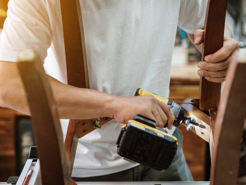 carpenter repair chair and using electric screwdriver at workshop, furniture restoration woodworking concept. selective focus