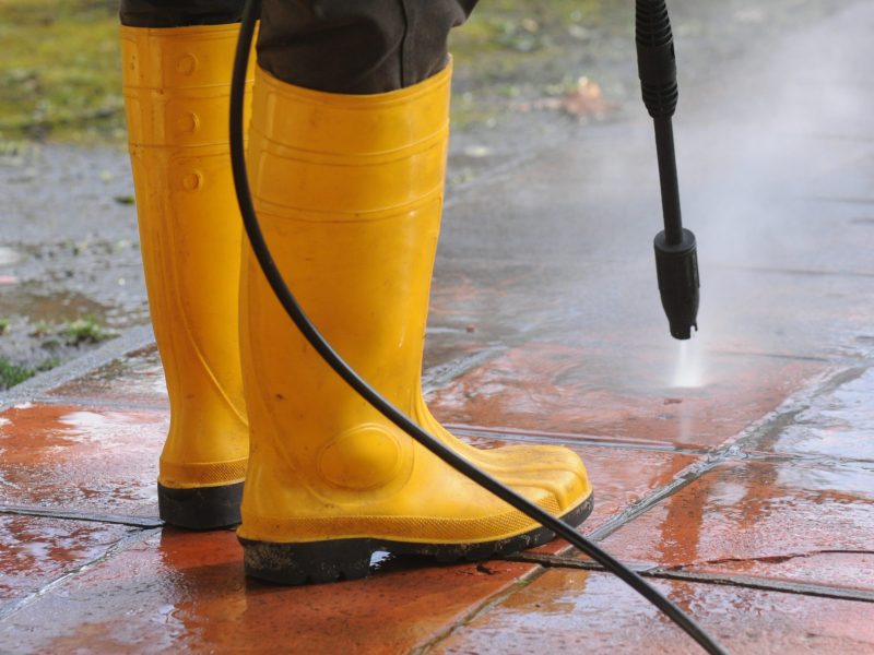 A person wearing yellow rubber boots with high-pressure water nozzle cleaning the dirt in the tiles